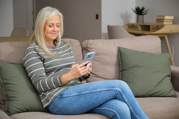 istock Smiling senior woman using smartphone at home on sofa browsing internet 2184533138