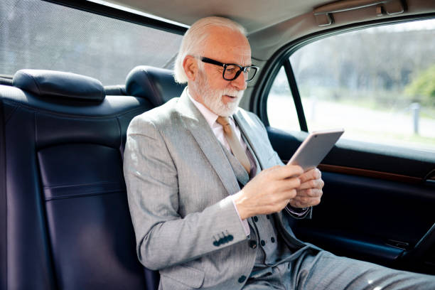 istock Portrait of senior smiling business man in formal clothes using digital tablet while sitting on back seat of luxury business car 2184533593