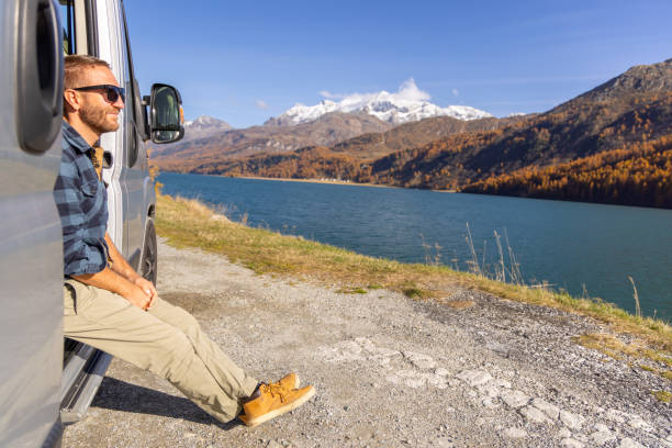 istock Man Enjoying Lakeside View from Camper Van Door 2184554193