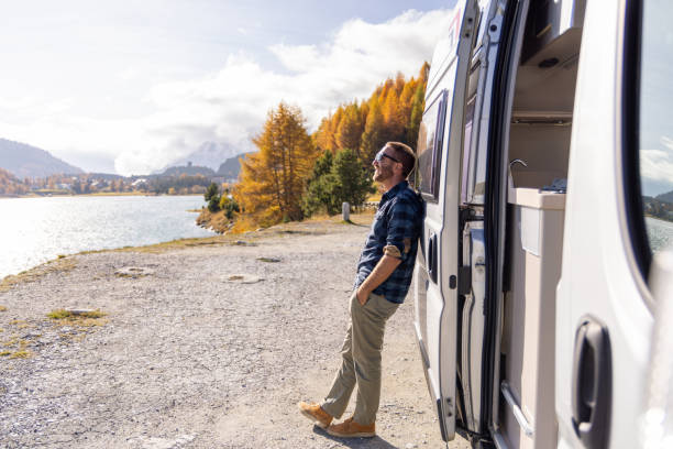istock Man Enjoying Lakeside View by Camper Van on a Sunny Autumn Day 2184554248