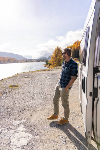 istock Man Enjoying Lakeside View by Camper Van on a Sunny Autumn Day 2184554335