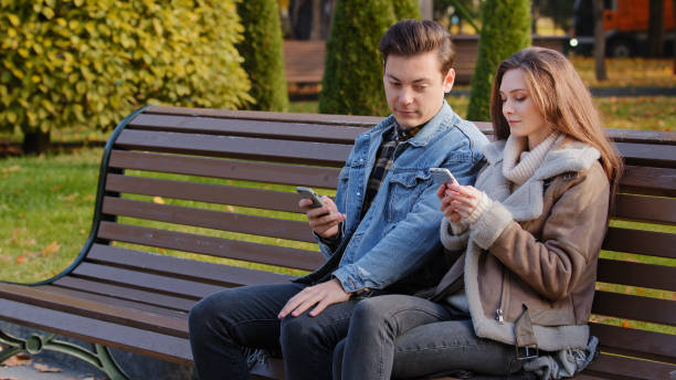istock Caucasian couple two young people partners sit on bench use phone cell gadgets scroll internet web pages check social networks show images each other spend time in city park suffer of mobile addiction 2184573544