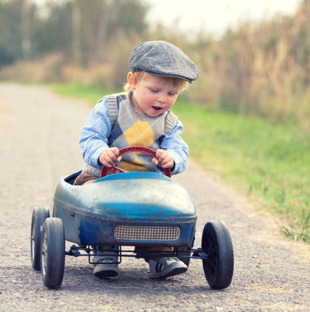 curious small boy is riding a retro pedal car in nature, happy childhood