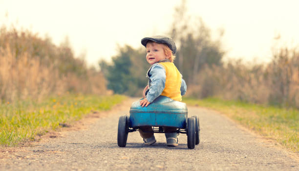 happy toddler is driving a retro toy car in nature, happy childhood