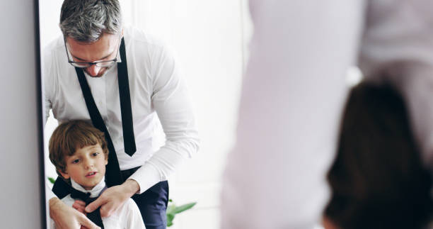 istock Father, child and help with tie by mirror for event preparation, learning or ready together in family home. Dad, kid and boy in formal necktie, clothes and dressing or wear with reflection of parent 2184577934