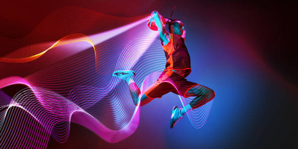 Dynamic image of young man, basketball player in motion during game against dark gradient background with abstract neon lines elements.