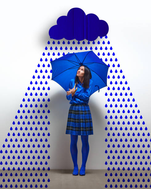 Woman dressed in blue, standing under blue umbrella with abstract rain cloud and raindrops. Sadness, loneliness. Contemporary art collage. Concept of psychology, feelings, mental health