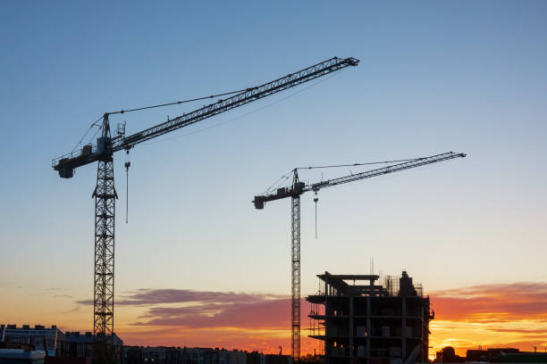 istock Tall construction cranes against the evening sky. There is an orange sunset stripe and a building under construction. Background. Landscape. 2184590016