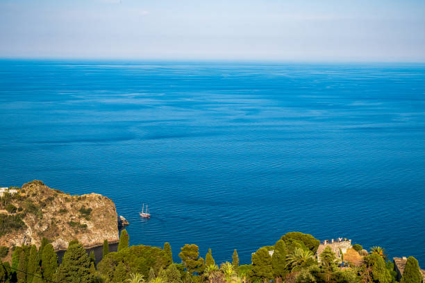 A panoramic view of the sea from the heights of Taormina, Sicily, with a peaceful coastal landscape and green hills in the foreground.