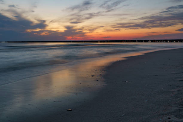 sunset over the sea horizon with blurred waves just off the shore and breakwaters in the background