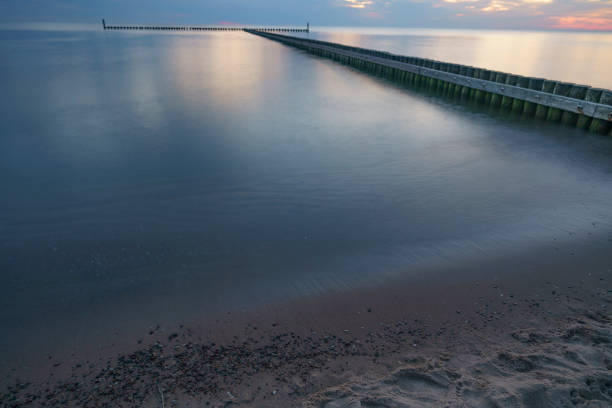 sunset over the sea horizon with blurred waves just off the shore and breakwaters in the background