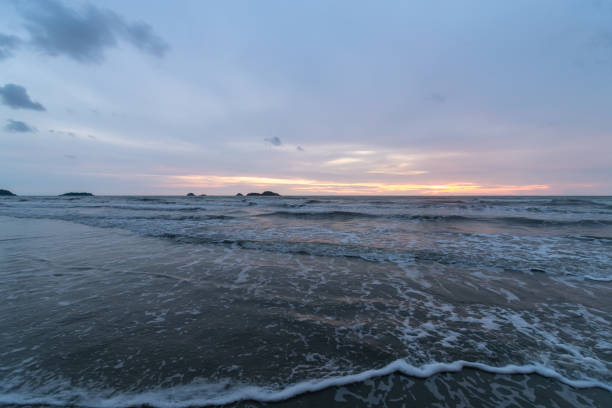 A serene coastal scene shows gentle waves on the shore and a stunning sunset reflecting on the waters surface