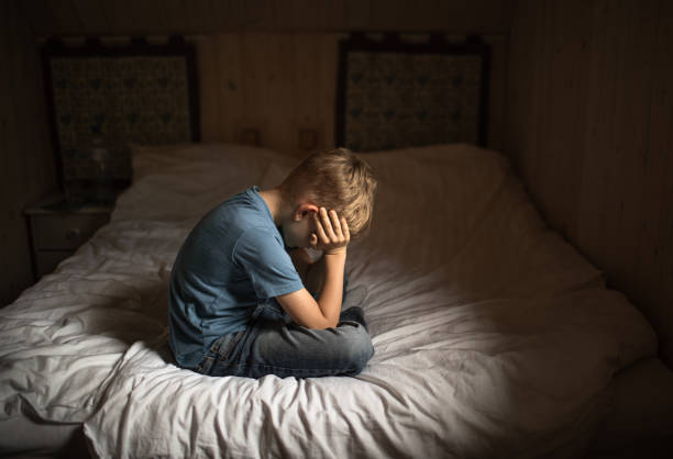istock Sad unhappy little boy at home sitting on bed with head down. 2184609213