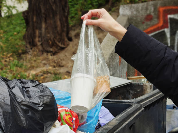 istock A human hand is throwing a transparent trash bag into a big black plastic garbage container on the street. The person takes out the trash, Holds a garbage bag by hand, and puts it in the trash can. 2184613129