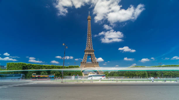 Eiffel Tower on Champs de Mars in Paris timelapse hyperlapse, France. Blue cloudy sky at summer day with green lawn and fountain with traffic around