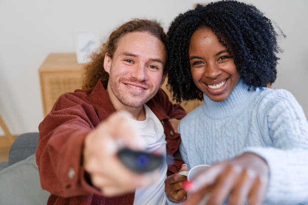 istock Happy couple watching tv, changing channels and pointing at screen 2184618908
