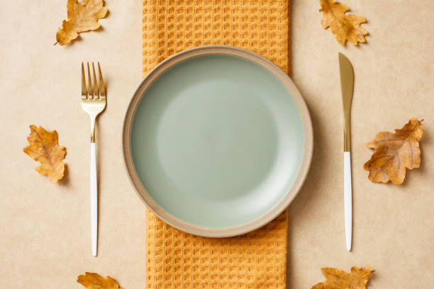 istock Elegant table setting with a pastel green plate on a textured yellow cloth, surrounded by dried autumn leaves. Ideal for fall decor, dining themes, and minimalist designs. 2184620574