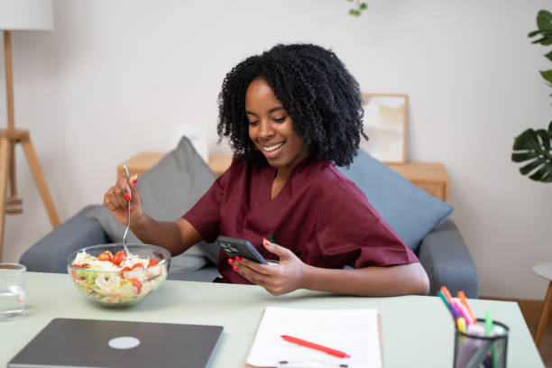 istock Young nurse eating salad and browsing smartphone during work break at home 2184621599