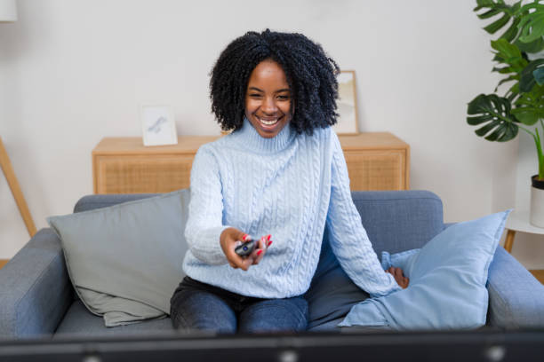 istock Young woman changing channels while watching tv on sofa at home 2184623210