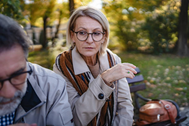 istock Senior woman appearing to criticize her husband while he sits thoughtfully on a park bench during autumn, suggesting tension or conflict in their relationship 2184623308