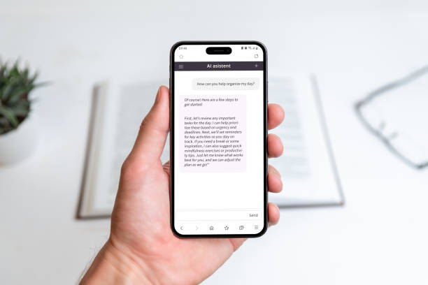 istock Hand holding AI assistant app on smartphone, helping organize daily tasks, improve productivity, and manage time effectively, background shows a workspace with book for focused planning 2184623362