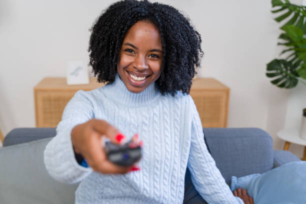 istock Smiling woman changing channels on the sofa with remote control 2184624129