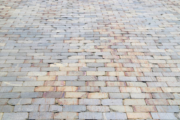 istock Old damaged sidewalk paved with gray and orange rectangular stone tiles with brown stains in perspective 2184628399