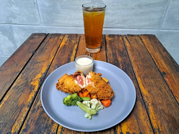 Chicken Cordon Bleu With Potato Wedges, Snow Peas, Brocolli, Carrot And Mushroom Sauce. Fresh Tea IcedIn Glass. Food And Drink Menu.