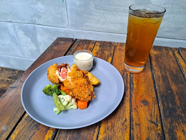 Chicken Cordon Bleu With Potato Wedges, Snow Peas, Brocolli, Carrot And Mushroom Sauce. Fresh Tea IcedIn Glass. Food And Drink Menu.