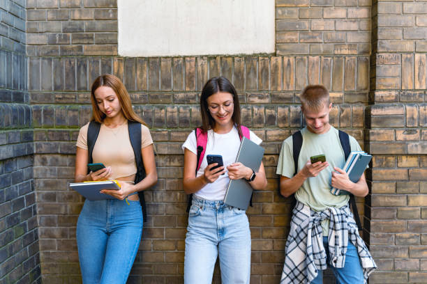 istock Three students focus on smartphones near brick wall 2184632170