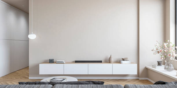 A modern minimalistic living room with an empty beige wall with copy space, a low white cabinet, coffee table, gray sofa, windows and decoration, a hallway