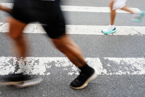 Unrecognizable NYC Marathon Runners' Legs Passing in Motion Blur This is a photo of the sneakers and legs of unrecognizable NYC Marathon runners running past a street crosswalk in a motion blur. new york marathon photos stock pictures, royalty-free photos & images