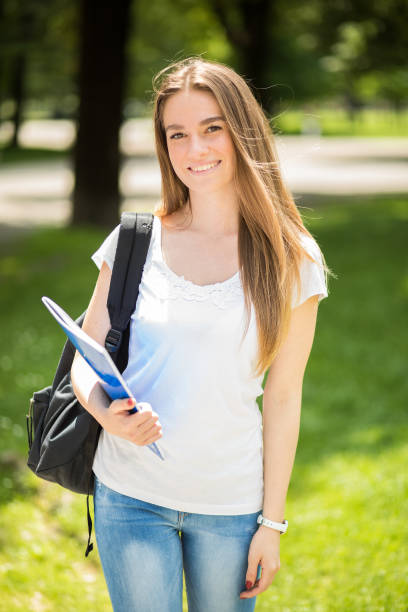 istock Smiling student girl walking in the park with backpack and book 2184634434