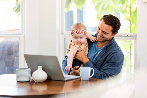 istock Businessman smiles while holding his daughter as he works from home 2184635585