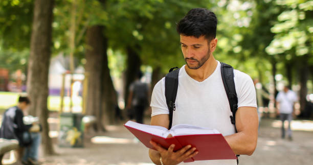 istock Young male student reading a book in a park during a break 2184635688