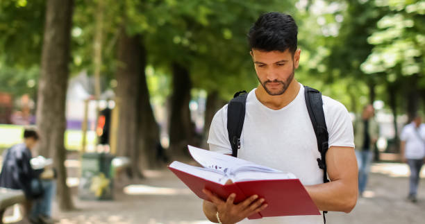 istock Young male student reading a book in a park 2184635697
