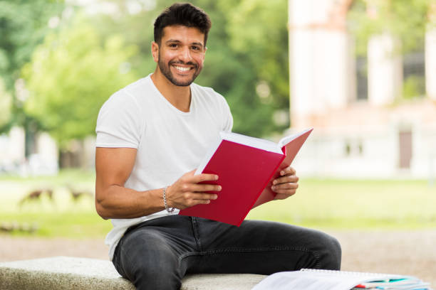 istock Young man reading a book and smiling at the university campus 2184635762