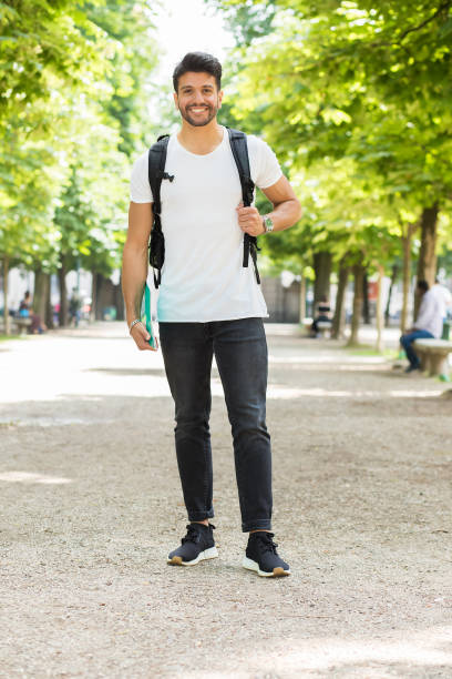 Smiling student walking in a park with backpack and books