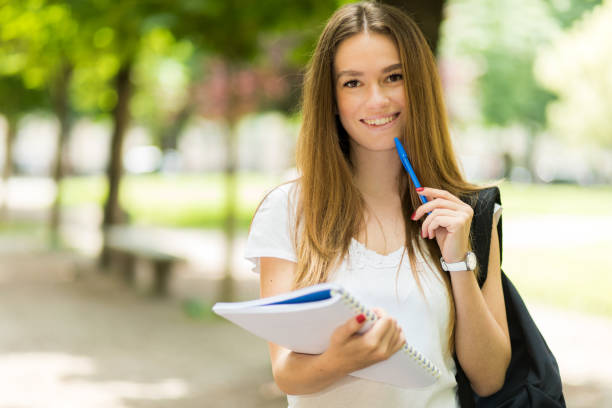 istock Smiling student holding a pen and a notebook at the park 2184635898