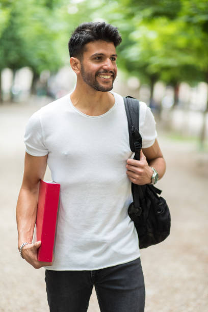 istock Smiling student walking in a park with backpack and book 2184635978