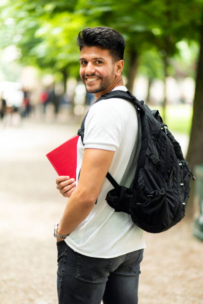 Young male student smiling at the camera while walking in a park