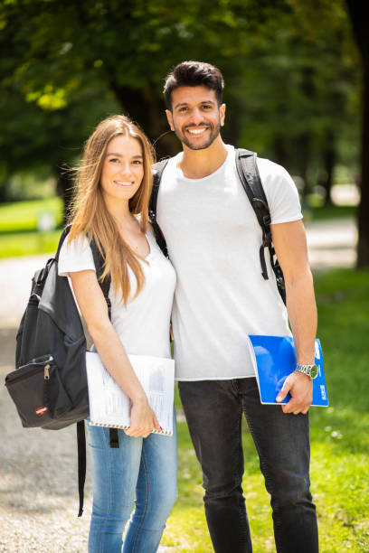 istock Two smiling students standing in a park with backpacks and books 2184637170