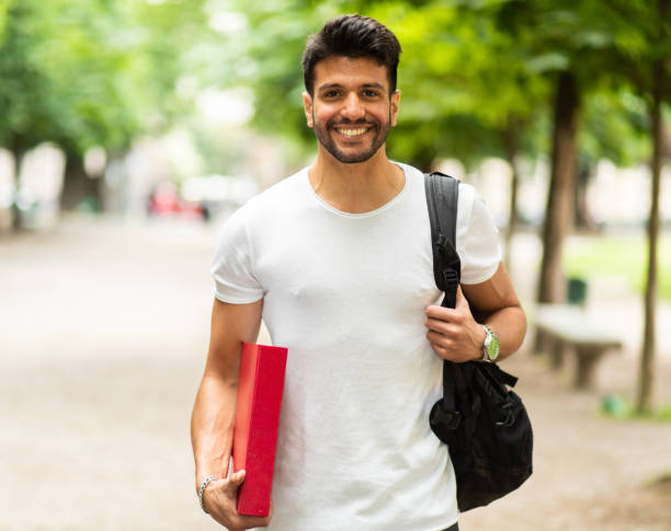 istock Young student smiling and walking in a park with backpack and books 2184637181