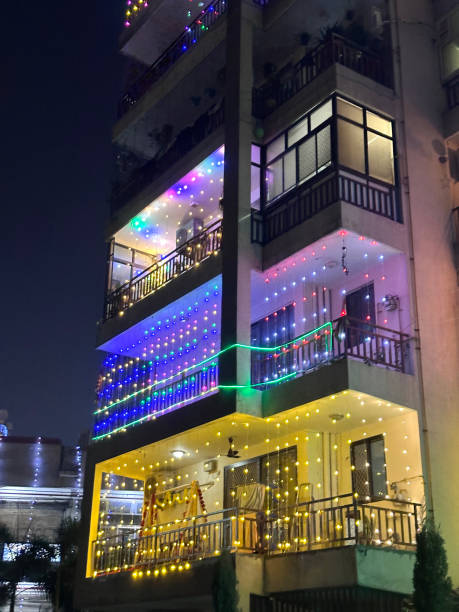 Stock photo showing close-up view of an apartment block decorated with multicolour fairy lights for Diwali the Hindu traditional festival of lights. imagen de primer plano de un bloque de apartamentos de gran altura en delhi, india, decorado con luces de hadas multicolores para diwali, festival tradicional hindú de luces, balcones de pisos de apartamentos, exterior del edificio, enfoque en primer plan