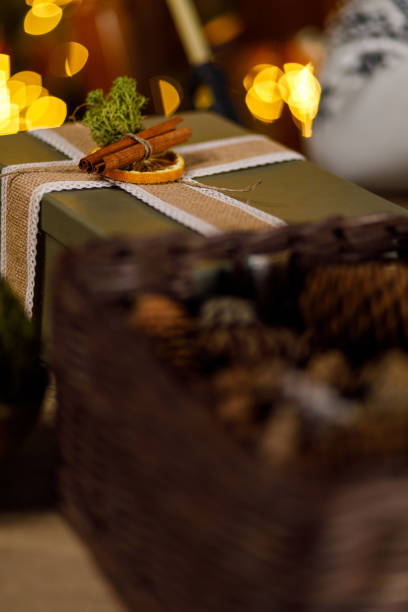 Close up shot of beautiful Christmas gift box with rustic decorations on top. Christmas tree branch, cinnamon sticks, dried orange slices and jute ribbon wrapped around it.