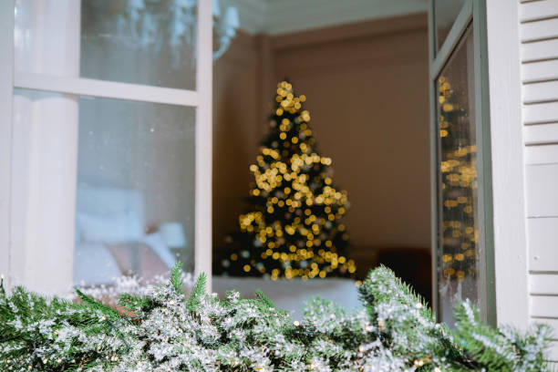 istock Holiday decorations and a glowing Christmas tree seen through a window 2184646836