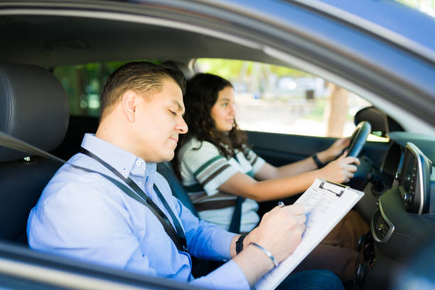 Focused driving instructor evaluating teenage student taking driving test while sitting in car