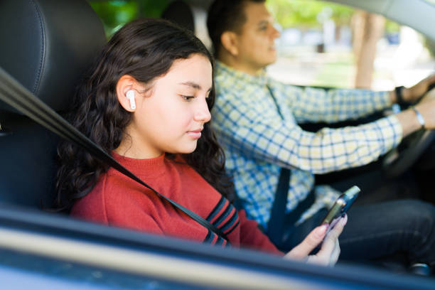 istock Hispanic daughter wearing earphones and using mobile phone while her father is driving a car 2184649114