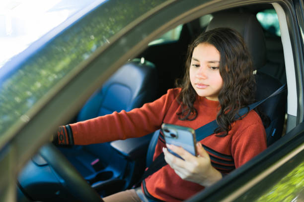 istock Teen driver using a mobile phone while driving her car, representing the dangers of distracted driving 2184653291