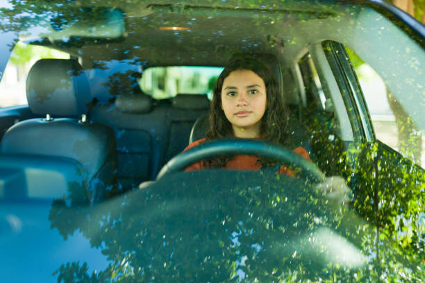 istock Teenager driving a car, seen through the windshield with a tree reflection, enjoying a sunny day 2184653589